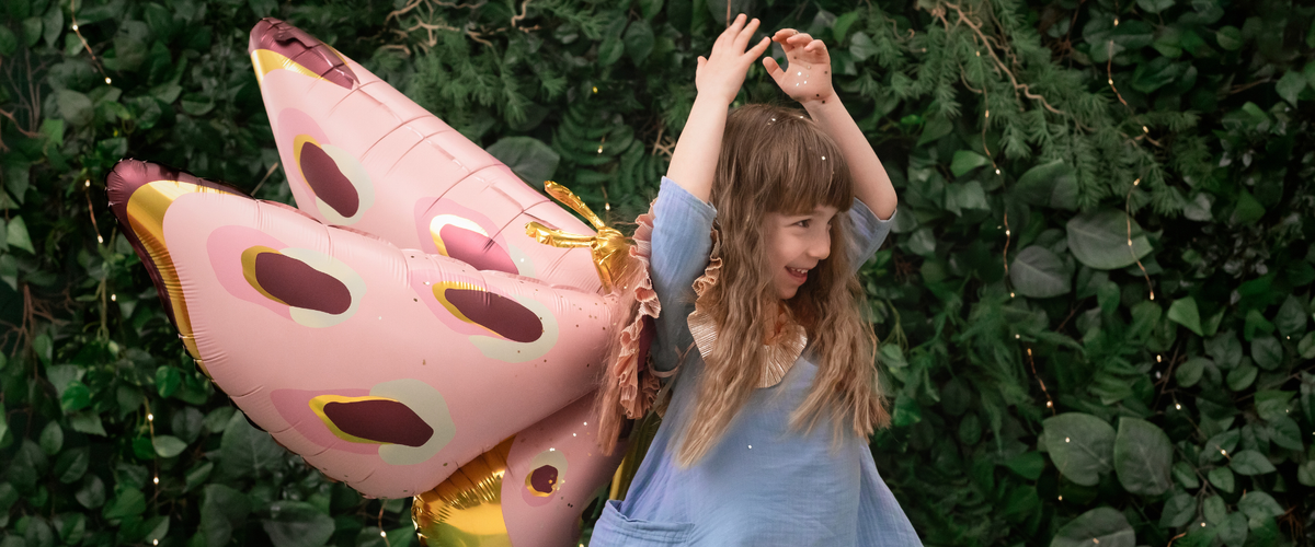 Little girl wearing butterfly balloon wings in the garden