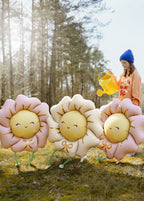 Three smiling flower-shaped balloons with 'legs' in a forest setting.