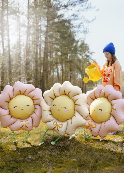 Three smiling flower-shaped balloons with 'legs' in a forest setting.