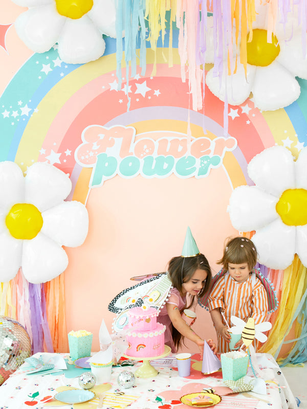 Children at a birthday party with a 'Flower power' backdrop featuring rainbows and flowers.