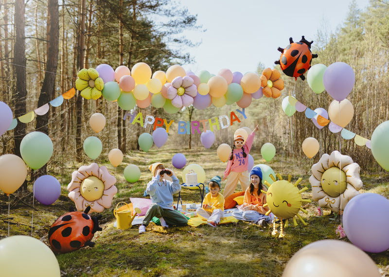 Outdoor birthday celebration with colorful balloons and decorations in a forest setting.