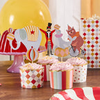 A set of circus-themed party cupcake toppers with various colorful designs, including an elephant, a clown, and a horse, displayed on a table with striped and polka dot patterned toppers.