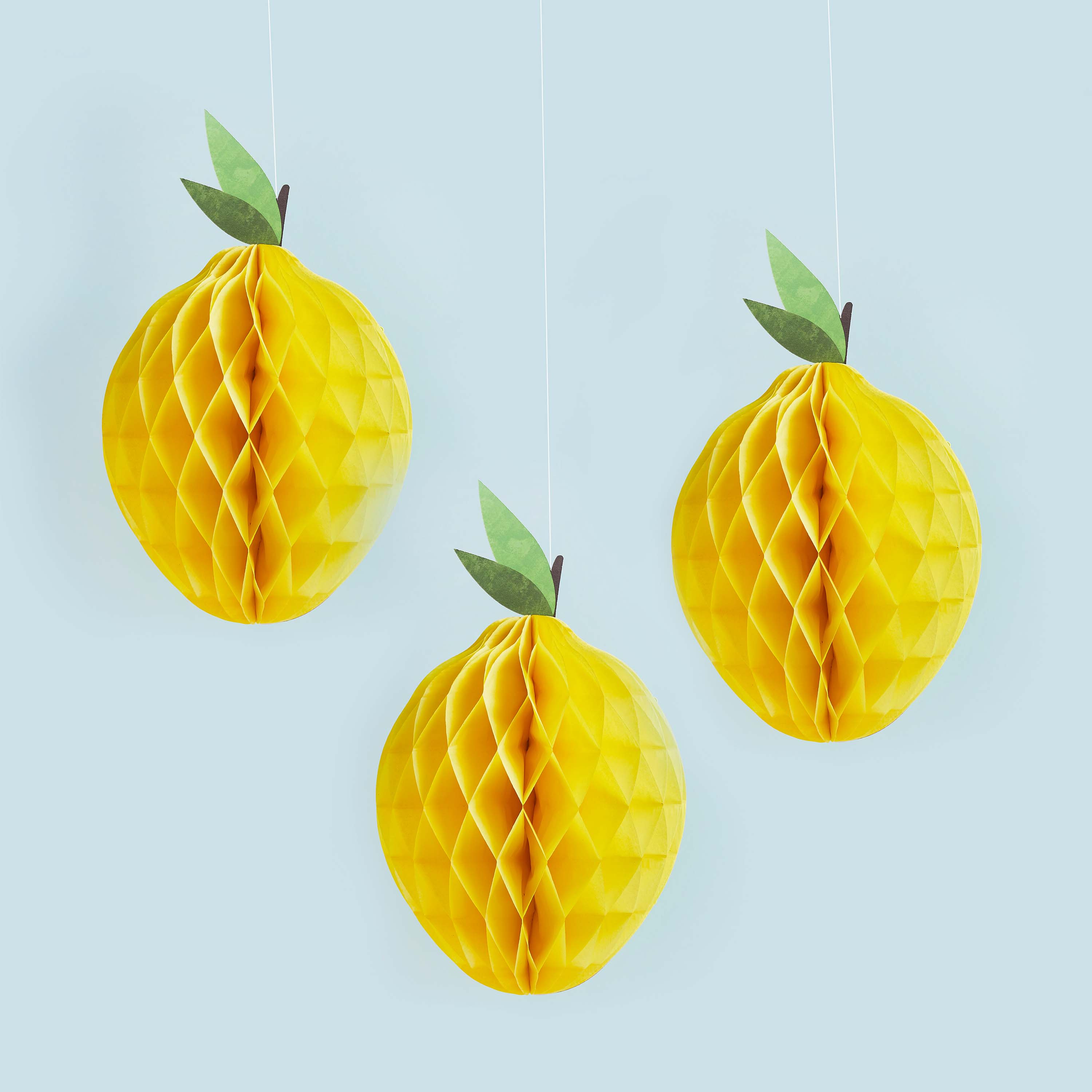 Three yellow honeycomb lemon decorations with green leaves on a light blue background
