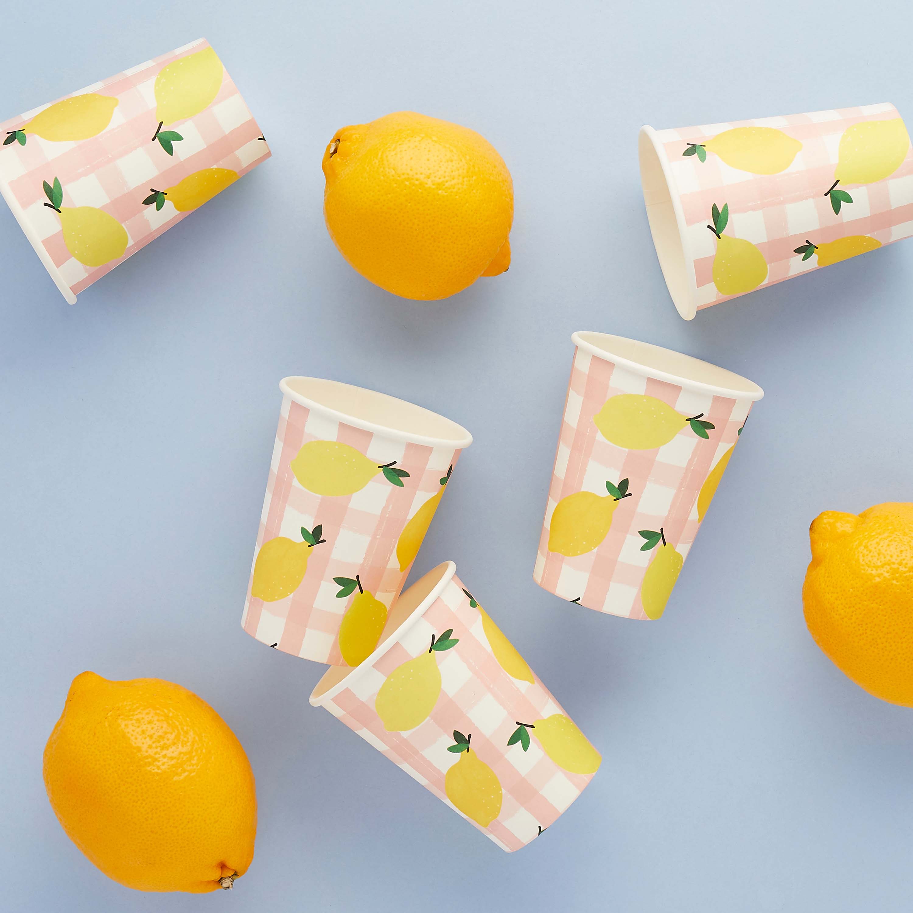 Paper cups with lemon pattern and lemons on a light blue background