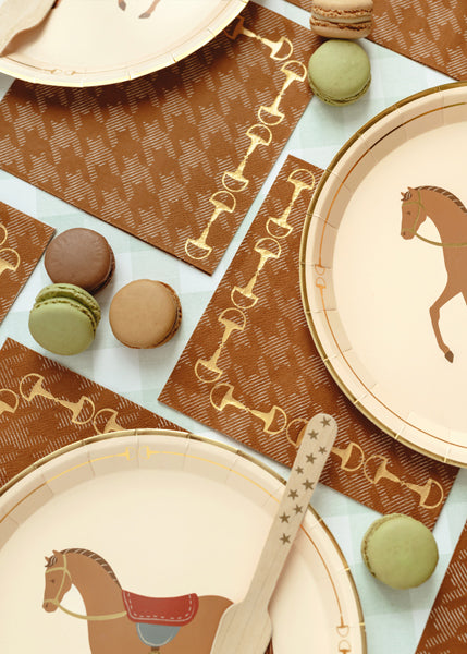Table setting with horse-themed plates, napkins, and macarons on a patterned tablecloth.