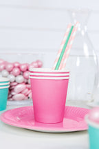 Pink cup with striped straw on pink plate with blurred candy background